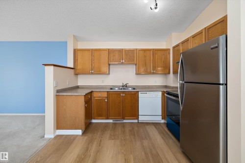 Kitchen featuring wood-finish cabinetry, laminate countertops, and stainless steel appliances including a refrigerator and range - 15016 134 Street, Edmonton, AB 