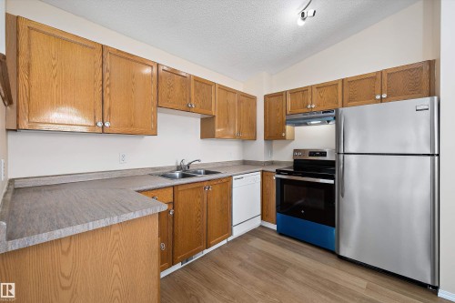 Kitchen featuring wood cabinetry, stainless steel refrigerator and range, dishwasher, double basin sink, and wood-finish flooring - 15016 134 Street, Edmonton, AB 