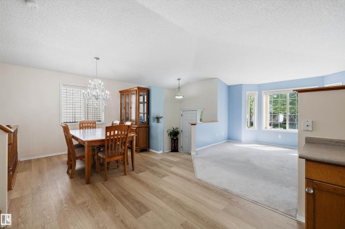 Open-concept interior featuring wood-finish flooring, a contemporary chandelier, a bay window with multiple panes, a built-in kitchen counter, and contrasting wall colors - 15016 134 Street, Edmonton, AB 
