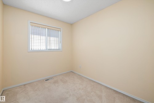 Neutral-toned room featuring a single window with horizontal blinds, light beige carpeting, and white baseboards - 15016 134 Street, Edmonton, AB 