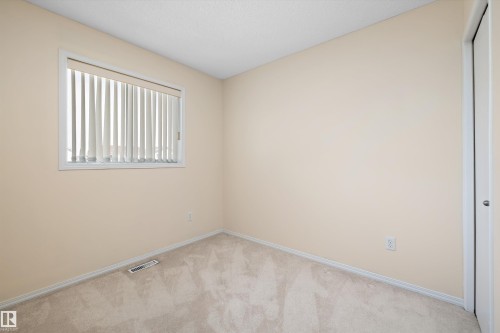 Carpeted room with a large window featuring vertical blinds - 15016 134 Street, Edmonton, AB 