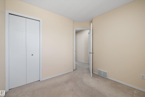 Carpeted room featuring a bifold closet with white panel doors, neutral wall paint, white trim, and a visible doorway - 15016 134 Street, Edmonton, AB 