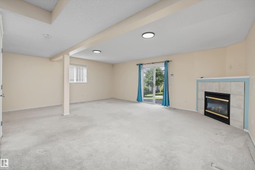 Spacious room featuring light-toned carpeting, a gas fireplace with a tiled surround, a sliding glass door, an additional window with blinds, and recessed lighting - 15016 134 Street, Edmonton, AB 