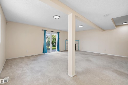 Expansive open-concept room featuring neutral carpet flooring, recessed lighting, and a sliding glass door providing outdoor access - 15016 134 Street, Edmonton, AB 