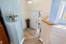 Entryway featuring wood-finish flooring, a white paneled door with sidelight, overhead lighting, and a light-toned staircase with a wood handrail - 15016 134 Street, Edmonton, AB 