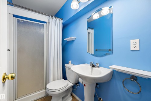 Bathroom featuring a stand-up shower with frosted glass enclosure, pedestal sink, and wall-mounted mirror - 15016 134 Street, Edmonton, AB 
