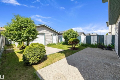 Spacious backyard featuring multiple concrete patio areas, a grass lawn, privacy fencing, and mature trees and shrubs - 15016 134 Street, Edmonton, AB 