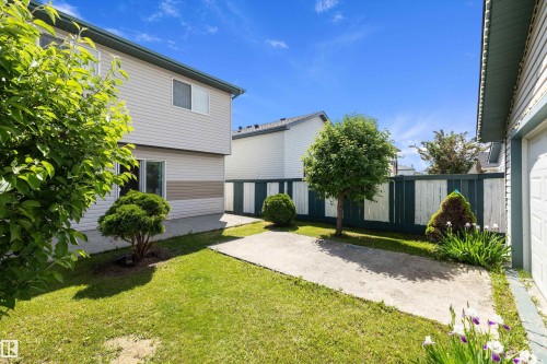 Expansive backyard featuring a manicured lawn, concrete patio, and a painted wood privacy fence - 15016 134 Street, Edmonton, AB 