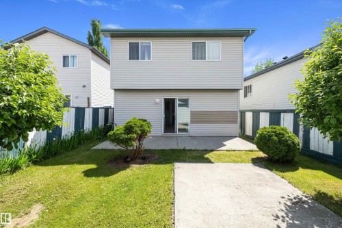 Exterior rear of a two-story residence featuring light-colored siding with an accent band, a green asphalt shingle roof, and a sliding patio door - 15016 134 Street, Edmonton, AB 