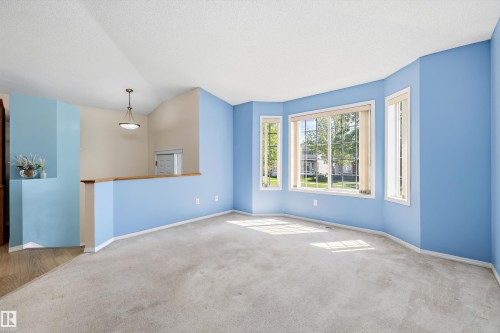 Spacious room featuring a multi-pane bay window, neutral carpet, and a half-wall with a wood-finish cap - 15016 134 Street, Edmonton, AB 