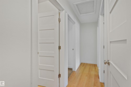 Hallway with light wood-finish flooring, white walls, and contemporary panel doors featuring brushed nickel hardware - 8212 148 Street Nw, Edmonton, AB 