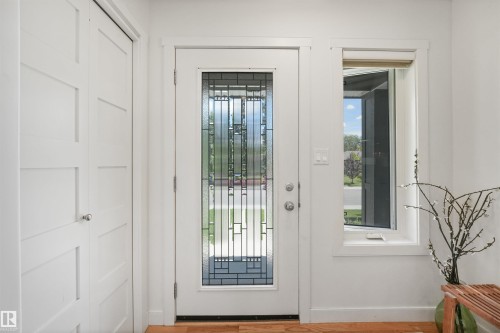 Entryway featuring a decorative glass panel door with a sidelight, white trim, and a flat-panel closet door with a chrome knob - 8212 148 Street Nw, Edmonton, AB 