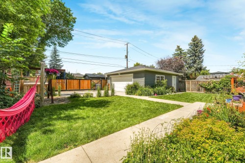 Spacious backyard featuring a detached garage with a white overhead door, a concrete pathway, and manicured lawn areas - 8212 148 Street Nw, Edmonton, AB 