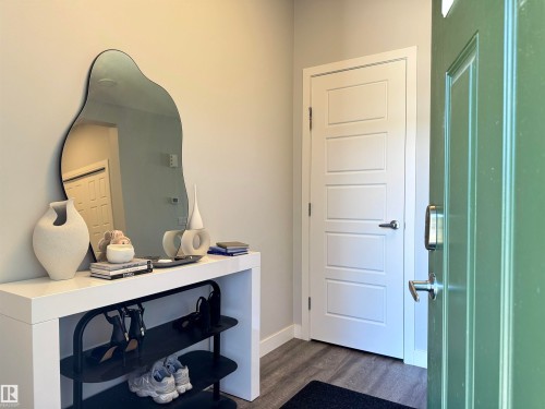 Entryway featuring a green paneled door with smart lock hardware, light gray walls, and wood-finish flooring - 7432 Elmer Road, Edmonton, AB 