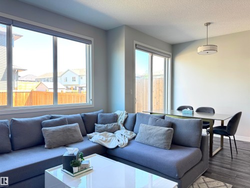 Open-concept living area featuring a large window, sliding glass door, and dark wood-finish flooring - 7432 Elmer Road, Edmonton, AB 