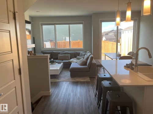 Open-concept living area with wood-finish flooring, large windows, and a sliding glass door to the exterior - 7432 Elmer Road, Edmonton, AB 
