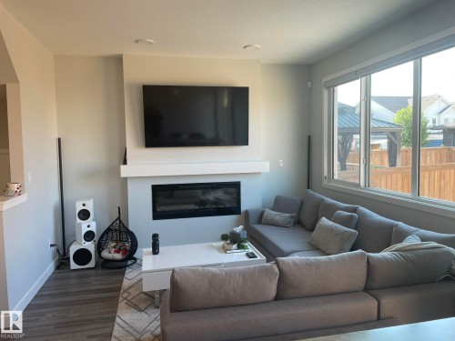 Living room featuring a built-in electric fireplace with a white mantel, wood-finish flooring, recessed lighting, and a large multi-pane window - 7432 Elmer Road, Edmonton, AB 
