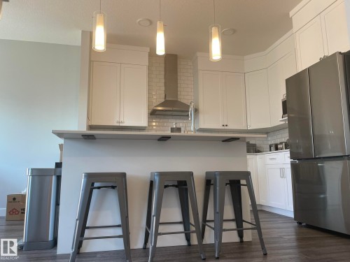 Modern kitchen featuring white shaker cabinetry, stainless steel appliances, a subway tile backsplash, and a central island with pendant lighting - 7432 Elmer Road, Edmonton, AB 