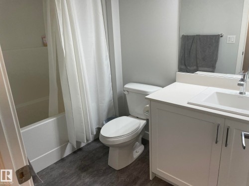 Modern bathroom featuring a white vanity with an integrated sink, polished chrome faucet, and a full-width mirror - 7432 Elmer Road, Edmonton, AB 