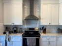 Modern kitchen featuring white shaker-style cabinetry, subway tile backsplash, stainless steel range hood, and light-toned countertops - 7432 Elmer Road, Edmonton, AB 