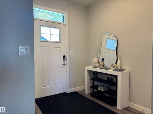Entryway featuring a paneled door with glass insert and transom window, light gray walls, wood-finish flooring, and a digital lock - 7432 Elmer Road, Edmonton, AB 
