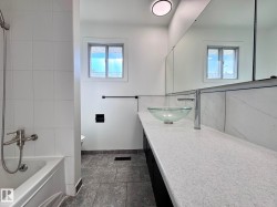 Bathroom featuring a contemporary vessel sink, stone-look countertop, large vanity mirror, white subway tile shower surround, and dark-toned floor tiles - 