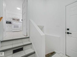 Staircase with tile treads and risers, leading to a kitchen featuring white cabinetry and a tile floor - 