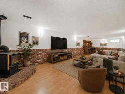 Spacious recreational area featuring wood-finish flooring, brick accent walls, and ceiling-mounted light fixtures - 