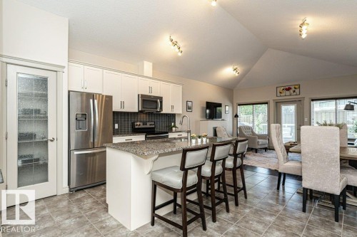 Open-concept kitchen featuring an island with counter seating, stainless steel appliances, a tile backsplash, and white cabinetry - 15 175 Mcconachie Drive, Edmonton, AB 