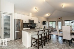 Open-concept kitchen featuring an island with counter seating, stainless steel appliances, a tile backsplash, and white cabinetry - 