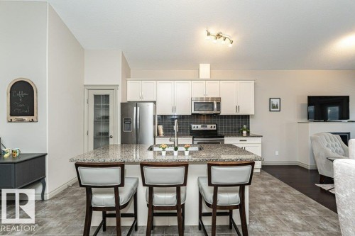 Kitchen island with a granite countertop, undermount sink, and integrated breakfast bar - 15 175 Mcconachie Drive, Edmonton, AB 
