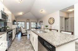 Open-concept kitchen featuring an island with an undermount sink, granite countertops, white cabinetry, and stainless steel appliances - 
