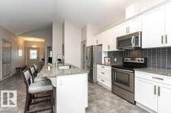Kitchen featuring a central island with an undermount sink, granite countertops, white cabinetry, stainless steel appliances, and a gray subway tile backsplash - 