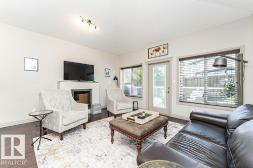 Living area featuring dark wood-finish flooring, light-colored walls, and a built-in fireplace with a television mounted above - 15 175 Mcconachie Drive, Edmonton, AB 