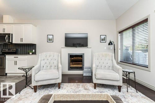 Living area featuring a dark wood-finish floor, a large window with horizontal blinds, and a built-in fireplace with a mantel - 15 175 Mcconachie Drive, Edmonton, AB 