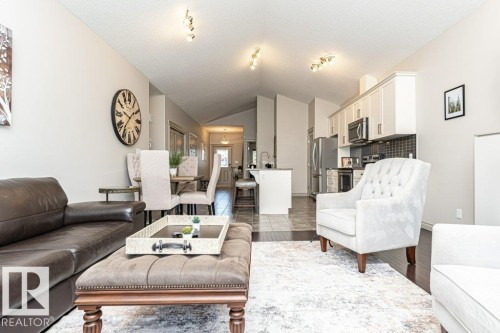Open-concept living space featuring vaulted ceilings, track lighting, dark wood-finish flooring, and a kitchen with stainless steel appliances and light-toned cabinetry - 15 175 Mcconachie Drive, Edmonton, AB 