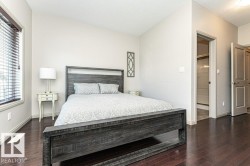 Bedroom featuring rich wood-finish flooring, light-toned walls, a window with horizontal blinds, and a doorway opening to a tiled shower enclosure - 