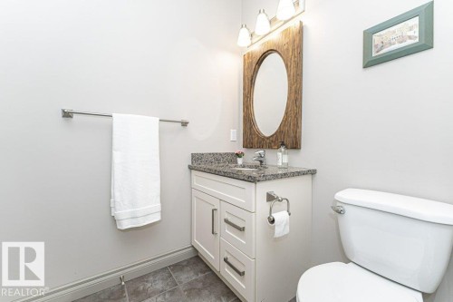 Bathroom featuring a white vanity with a granite-style countertop, undermount sink, and a rustic-framed oval mirror - 15 175 Mcconachie Drive, Edmonton, AB 