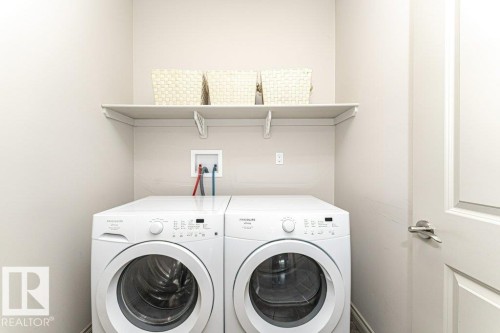 Dedicated laundry area featuring a built-in shelf, light-toned walls, and a white paneled door with chrome hardware - 15 175 Mcconachie Drive, Edmonton, AB 