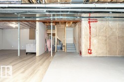 Spacious lower level featuring wood-finish flooring, exposed ceiling joists and ductwork, a partially finished area with white panel walls, and a concrete floor area - 