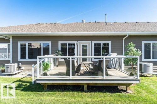 Rear exterior with a wood-finish deck featuring glass panel railings, a white framed door, and multiple white framed windows - 15 175 Mcconachie Drive, Edmonton, AB 