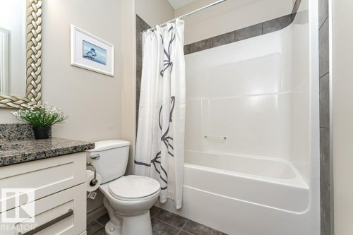 Bathroom featuring a white vanity with a dark speckled countertop, a toilet, and a white tub with a shower curtain - 15 175 Mcconachie Drive, Edmonton, AB 