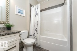 Bathroom featuring a white vanity with a dark speckled countertop, a toilet, and a white tub with a shower curtain - 