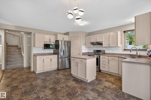 Kitchen featuring tile flooring, neutral cabinetry, a center island, stainless steel appliances, and a modern chandelier - 13406 32A Street, Edmonton, AB 