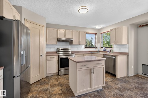 Kitchen featuring light-toned cabinetry, stainless steel appliances, a central island, tiled flooring, and dual windows - 13406 32A Street, Edmonton, AB 