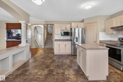 Kitchen featuring a central island with storage, stainless steel appliances, light cabinetry, and patterned floor tiling - 13406 32A Street, Edmonton, AB 