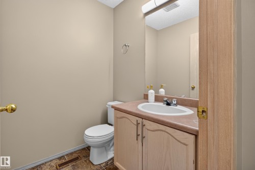 Bathroom vanity featuring a built-in sink, wood-finish cabinetry with silver hardware, and a wall-mounted mirror with overhead lighting - 13406 32A Street, Edmonton, AB 