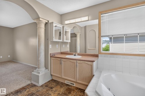 Bathroom vanity featuring a single basin sink, light wood-finish cabinetry, and a large mirror - 13406 32A Street, Edmonton, AB 