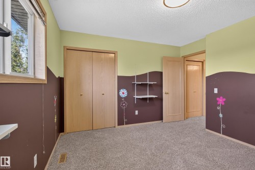 Carpeted room featuring a window with wood trim, wood-finish bi-fold closet doors, and light wood-finish interior doors - 13406 32A Street, Edmonton, AB 