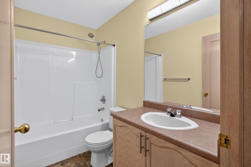 Bathroom featuring a white bathtub and shower surround, chrome fixtures, a vanity with a laminate countertop, and wood-finish cabinetry - 13406 32A Street, Edmonton, AB 